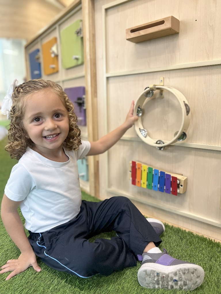 La música despierta el interés de una pequeña, que sonrie feliz con instrumentos en la Preprimaria APDE Connections Cayalá